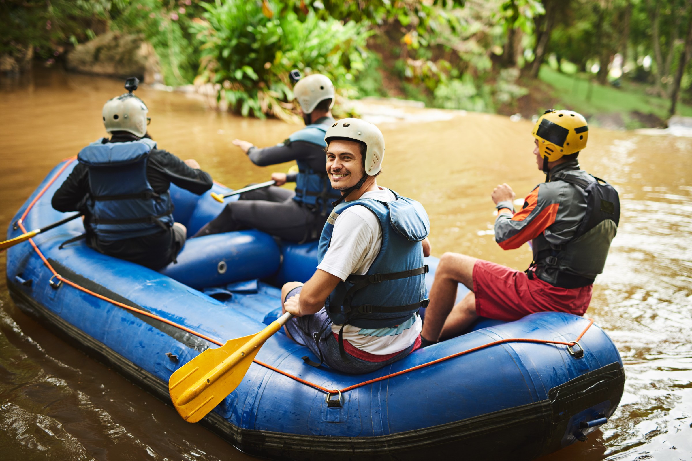 And so it begins…. High angle portrait of a handsome young man and his friends sitting in their white water raft.